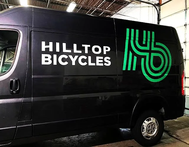 Black Ram ProMaster van wrapped with the white Hilltop Bicycles wordmark and a large green H/B monogram
