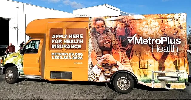 Orange MetroPlus Health mobile outreach vehicle wrapped with a family photo and Apply Here For Health Insurance messaging