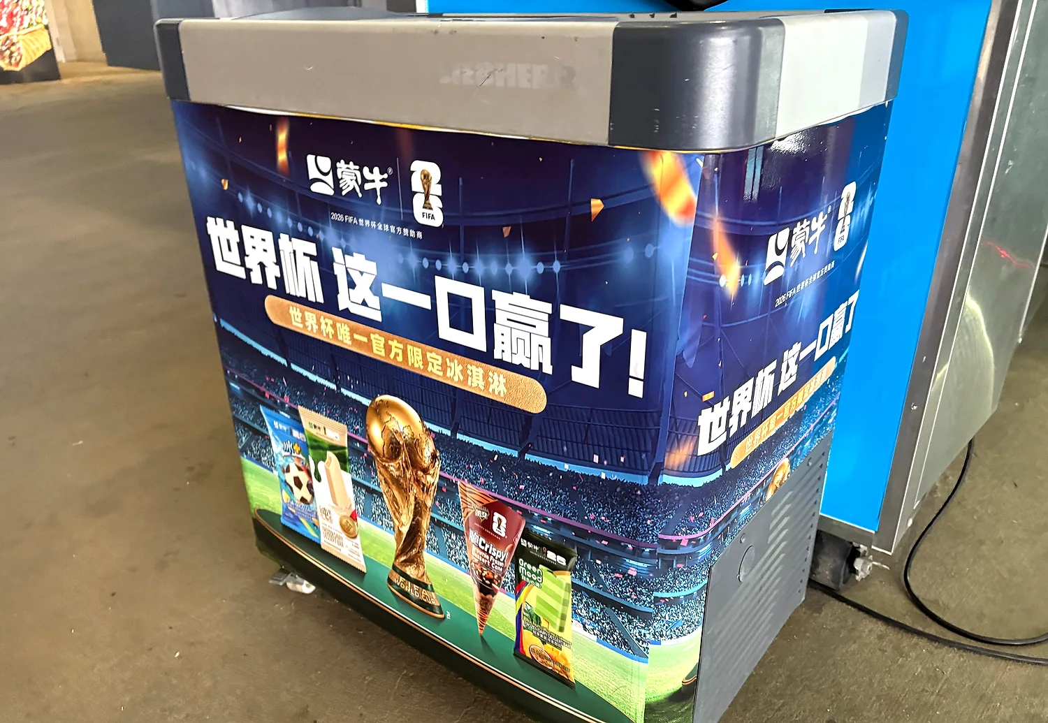 Promotional freezer cooler wrapped with World Cup stadium graphics, the trophy and beverage products